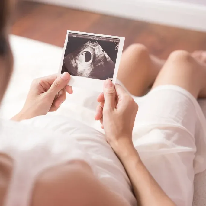 Pregnant asian woman looking at ultrasound scan of baby and touching her belly, close up of scan