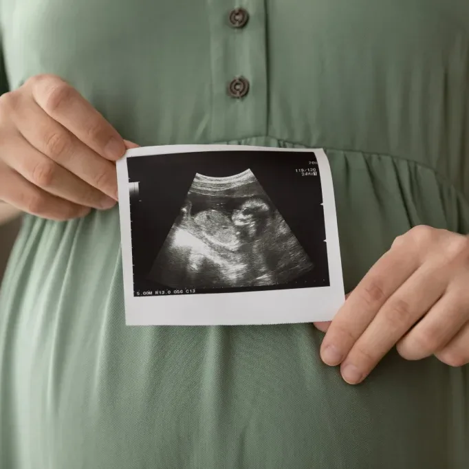 Prenatal ultrasound screening. Cropped close up shot of young pregnant female holding sonogram picture of unborn baby inside her big belly. Happy expectant mom showing fetus usi scan image to camera